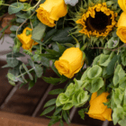 Vibrant bouquet with yellow roses, sunflowers, and lush green leaves in a close-up floral arrangement.