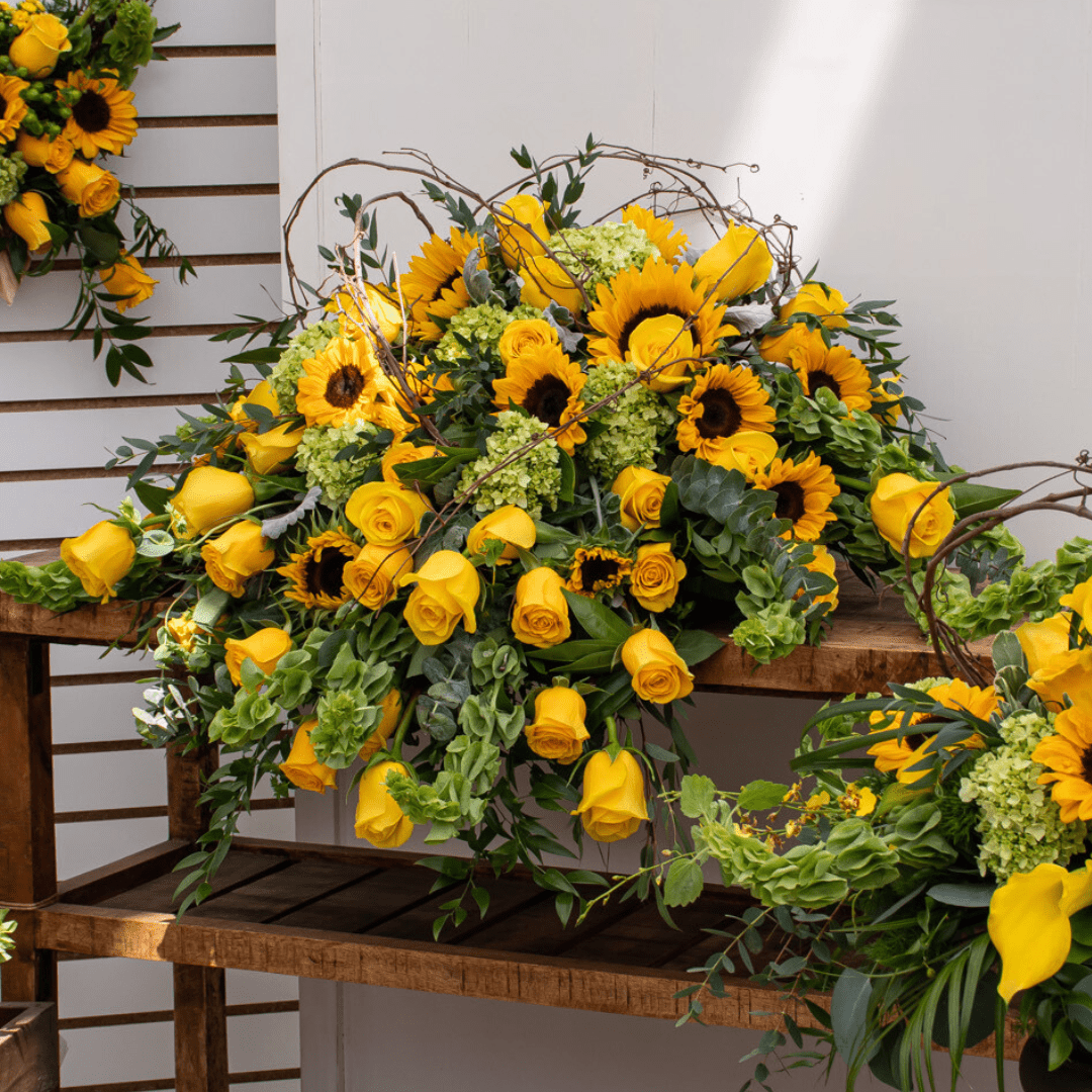Yellow roses and sunflowers arranged beautifully on a wooden table with green foliage.