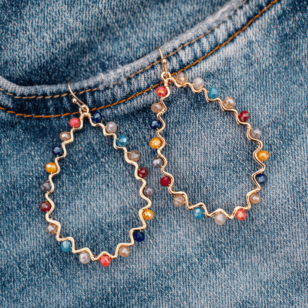 Colorful beaded teardrop earrings on denim fabric background, showcasing boho-chic jewelry style.