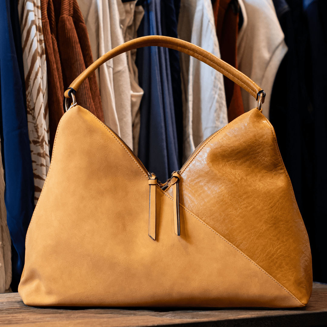 Elegant brown leather handbag displayed in front of various hanging clothes in a boutique setting.