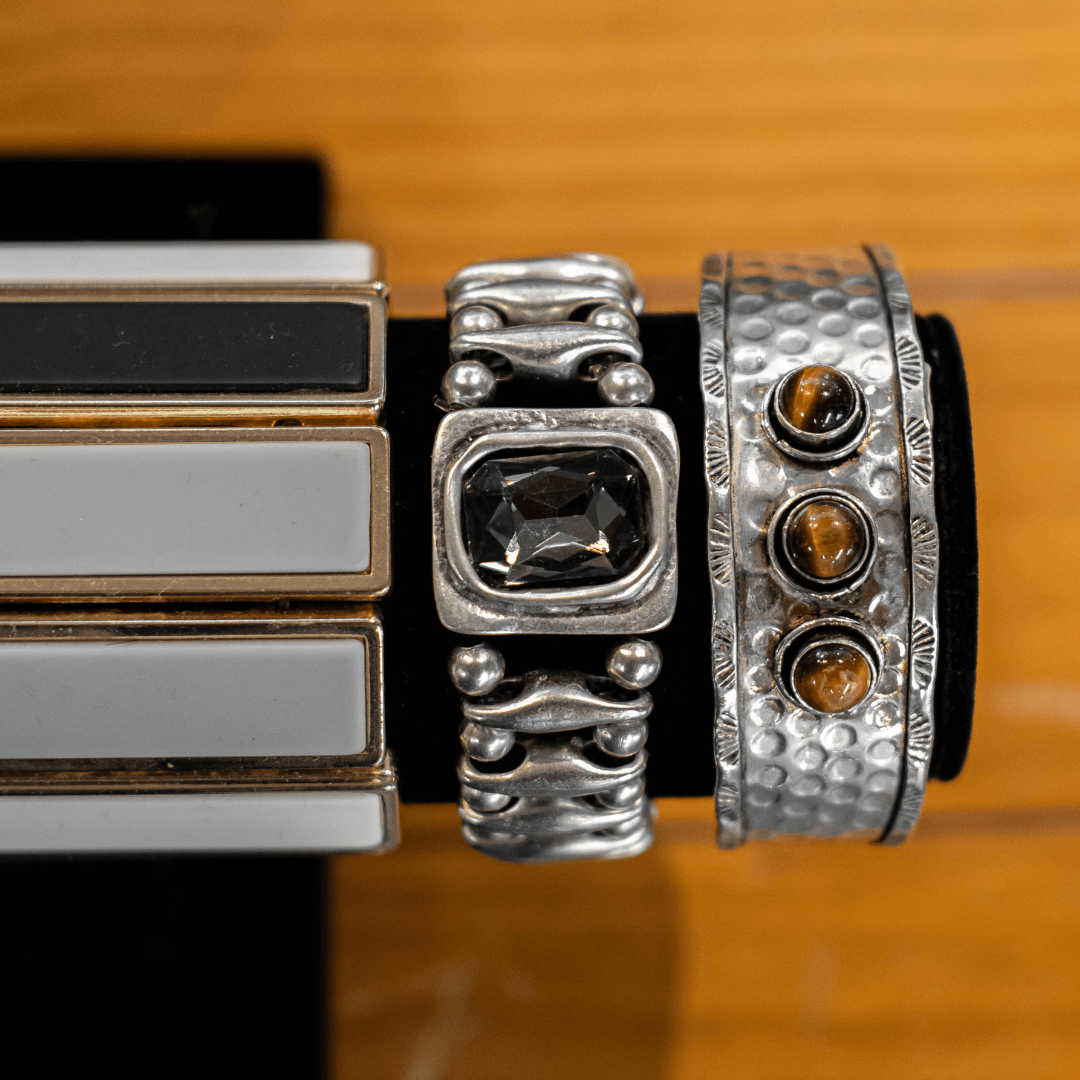 Variety of elegant bracelets featuring black gemstones and textured metal design, displayed on a black stand.