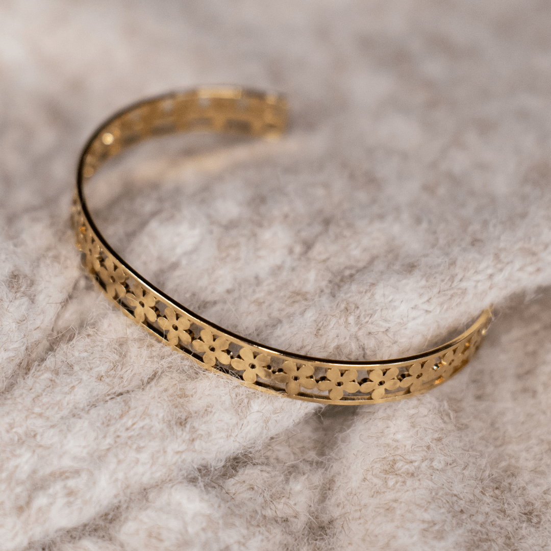 Elegant gold bracelet with floral cutouts on a soft beige fabric background.