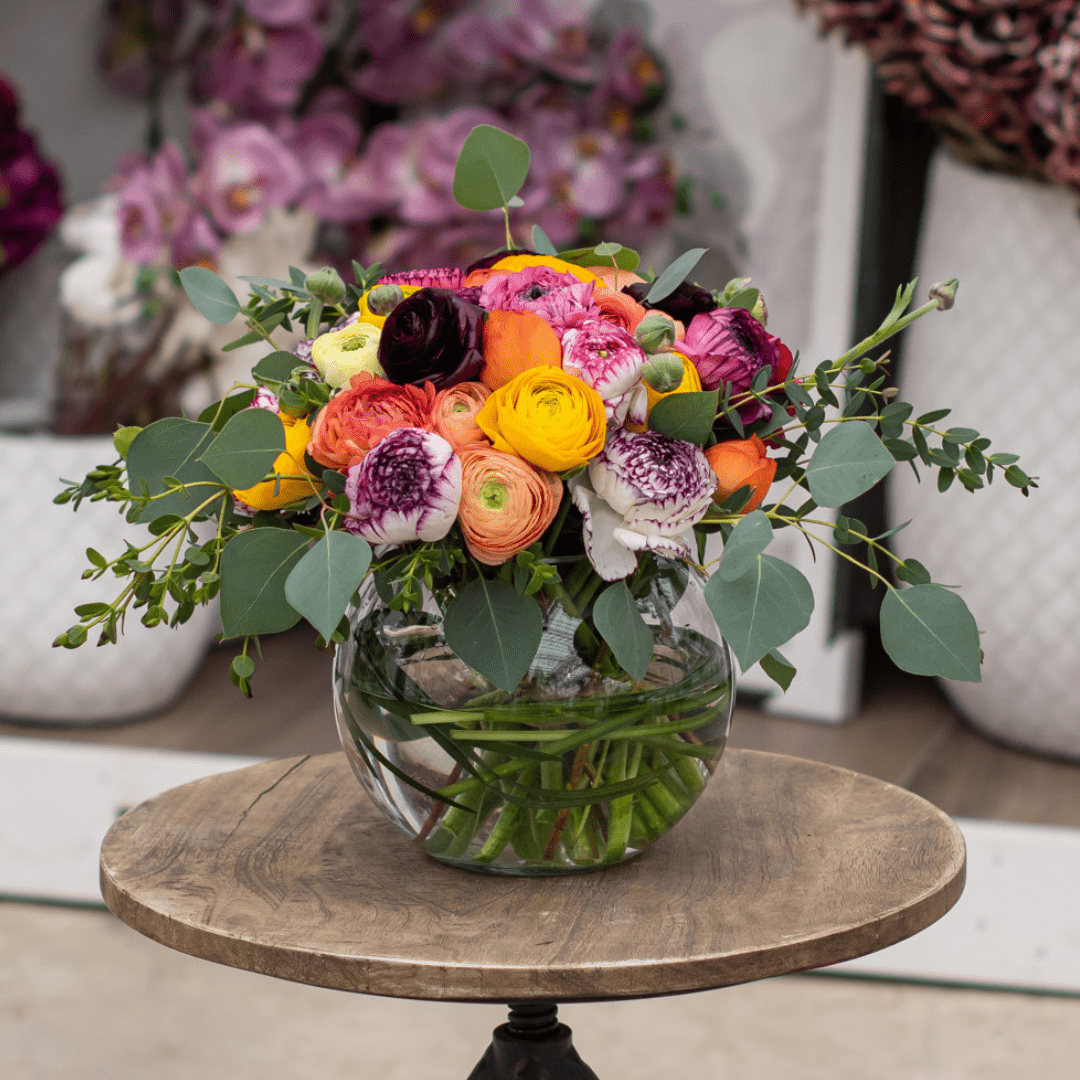 Vibrant flower arrangement with roses and greenery in a glass vase on a wooden table.