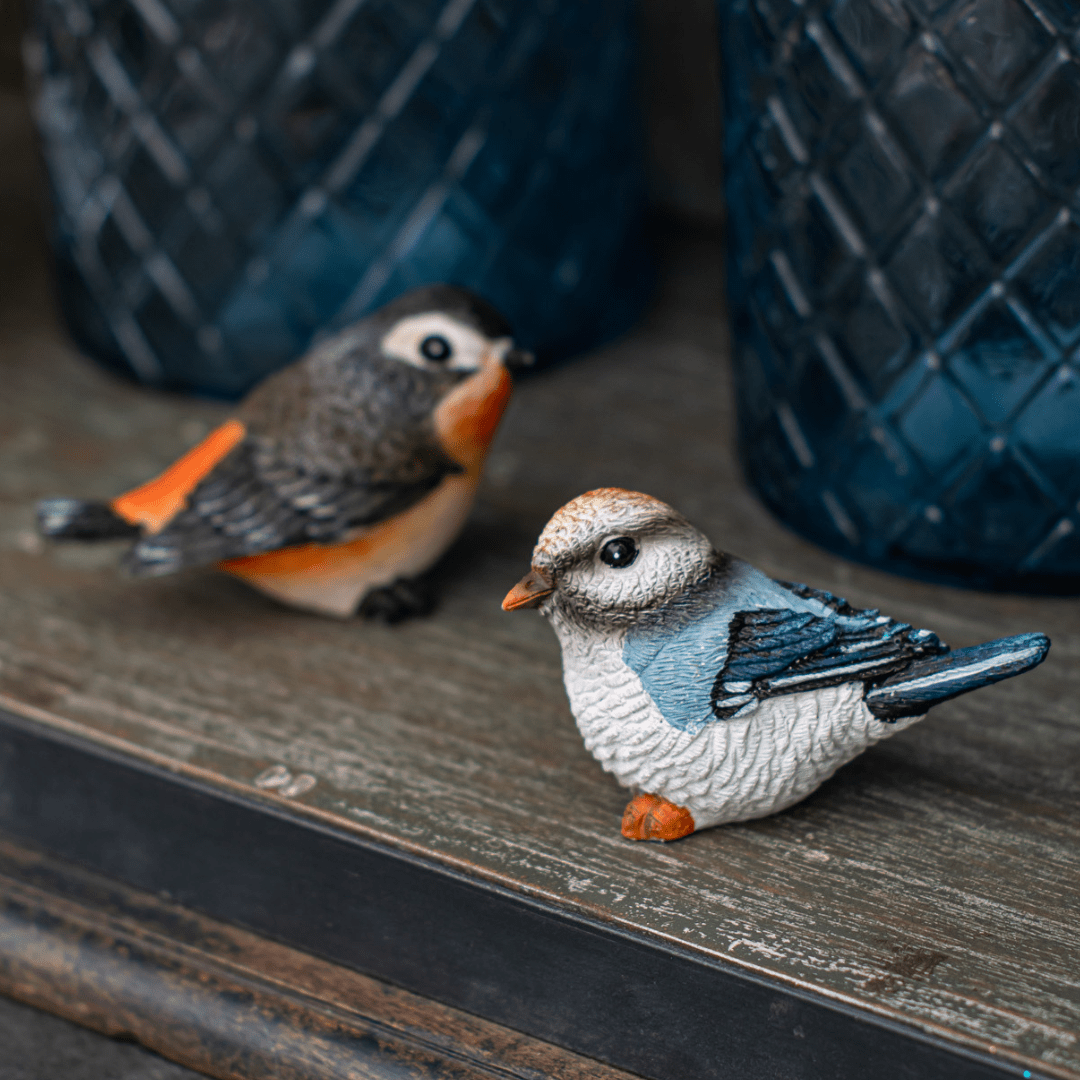 Colorful ceramic bird figurines on a wooden shelf with blue vases in the background.