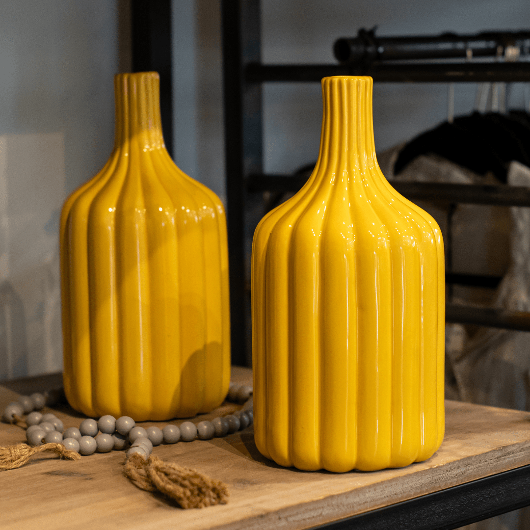 Two tall yellow ceramic vases with ribbed design on a wooden table with decorative beads.