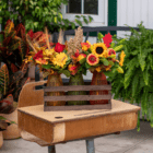 Autumn floral arrangements in vases on a wooden desk, surrounded by vibrant fall foliage and greenery.