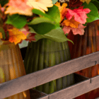 Autumn floral arrangement in colorful vases on a wooden rack, featuring vibrant leaves and blooms.