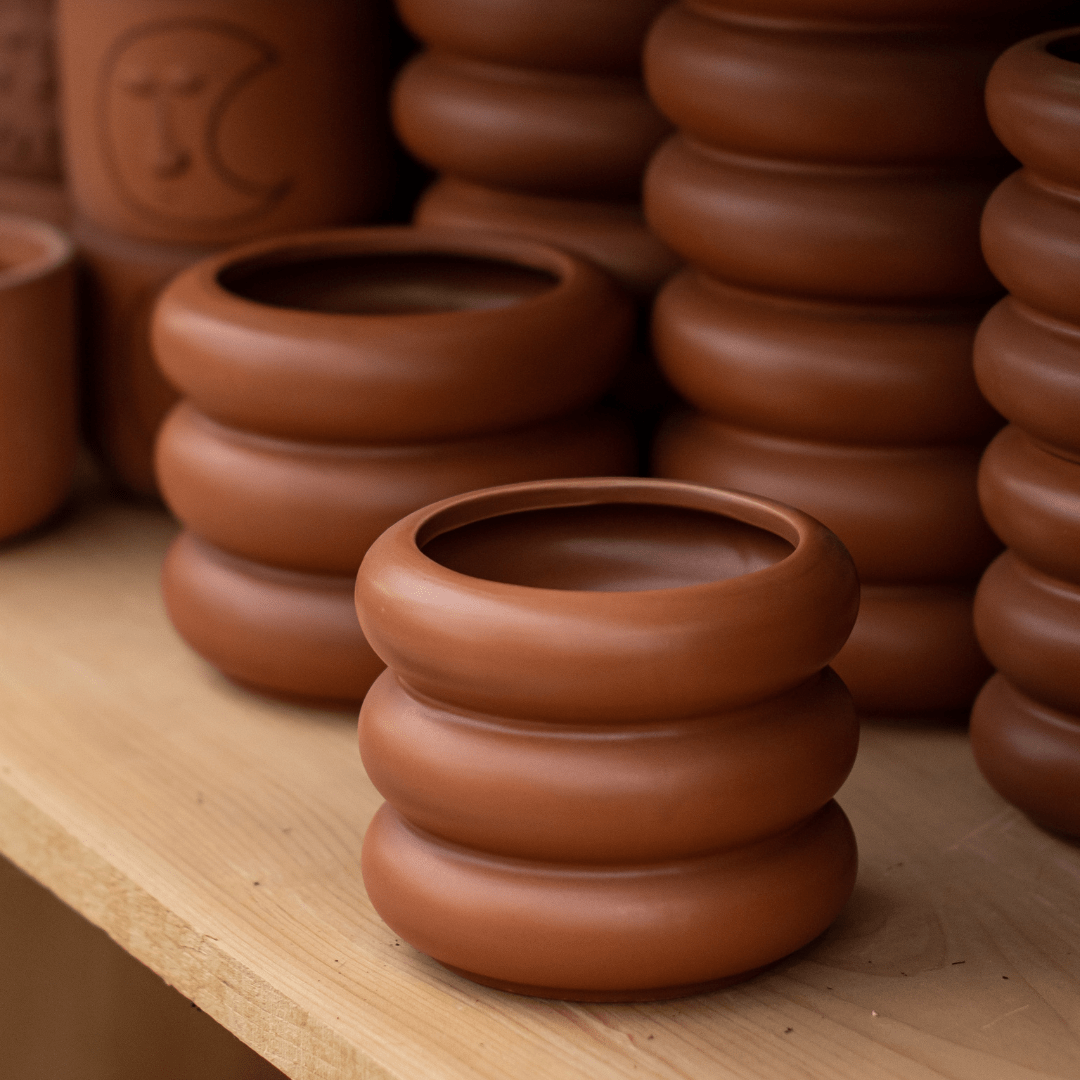 Handcrafted stacked clay pots on a wooden shelf, showcasing artistic pottery design and natural earth tones.