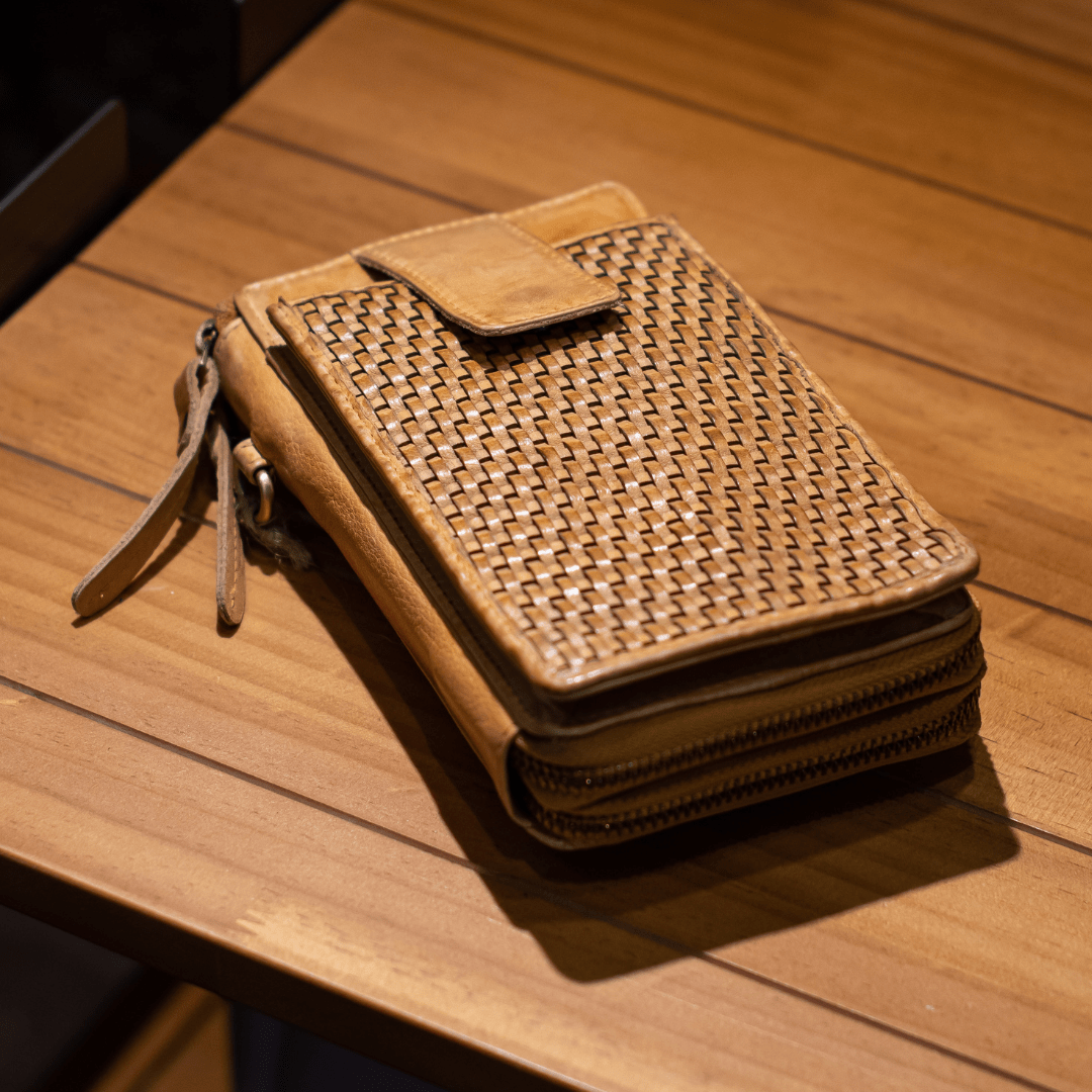 Woven leather wallet on a wooden table, featuring zippers and straps for stylish organization.
