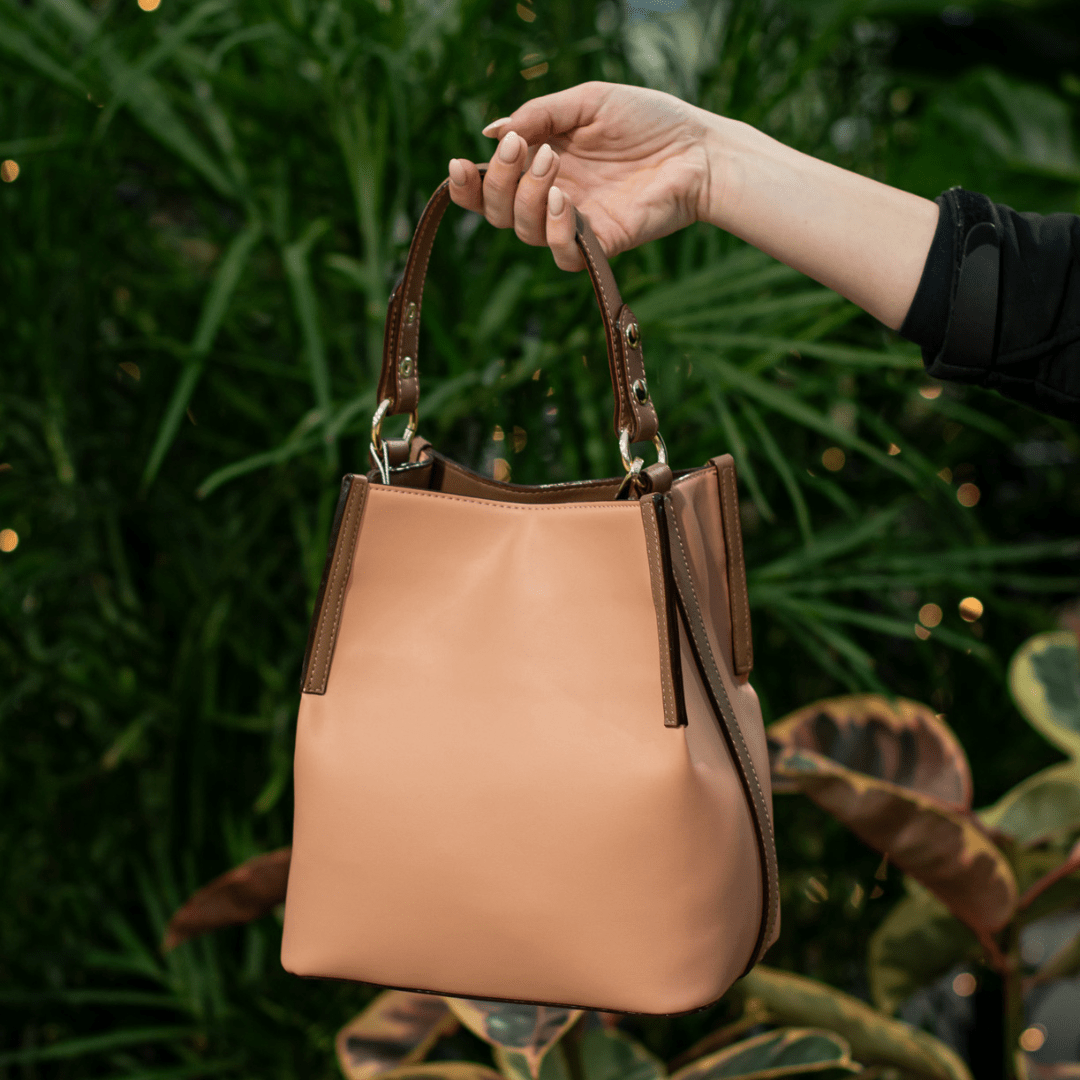 Stylish brown handbag held against a leafy green background, showcasing fashion elegance and design.