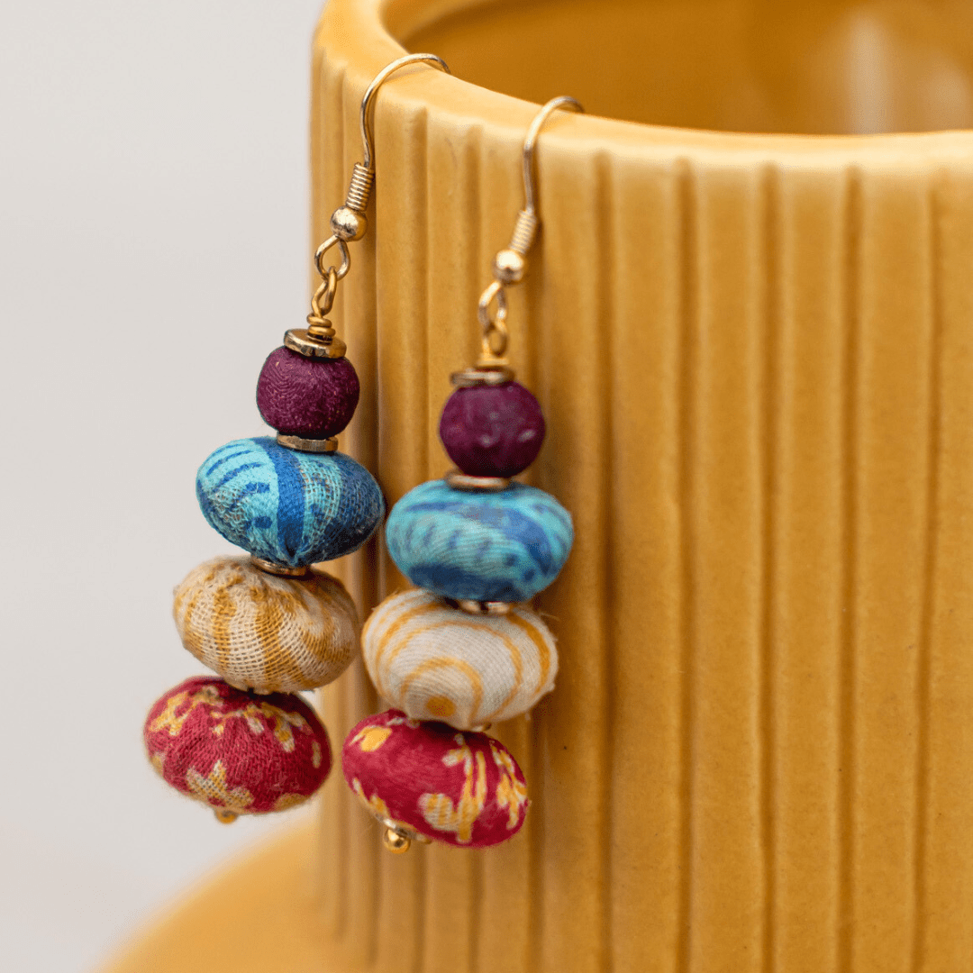 Colorful, handcrafted fabric bead earrings hanging on a textured surface. Unique fashion accessory.