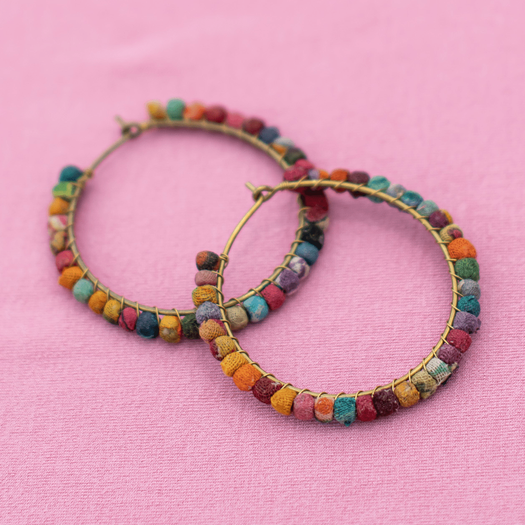 Colorful hoop earrings with beaded accents on a pink fabric background.
