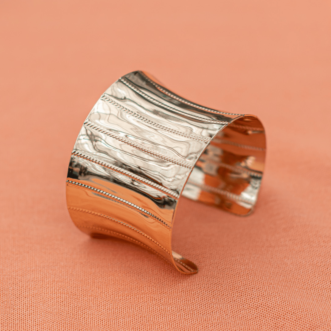 Elegant silver cuff bracelet with textured design on a peach background.