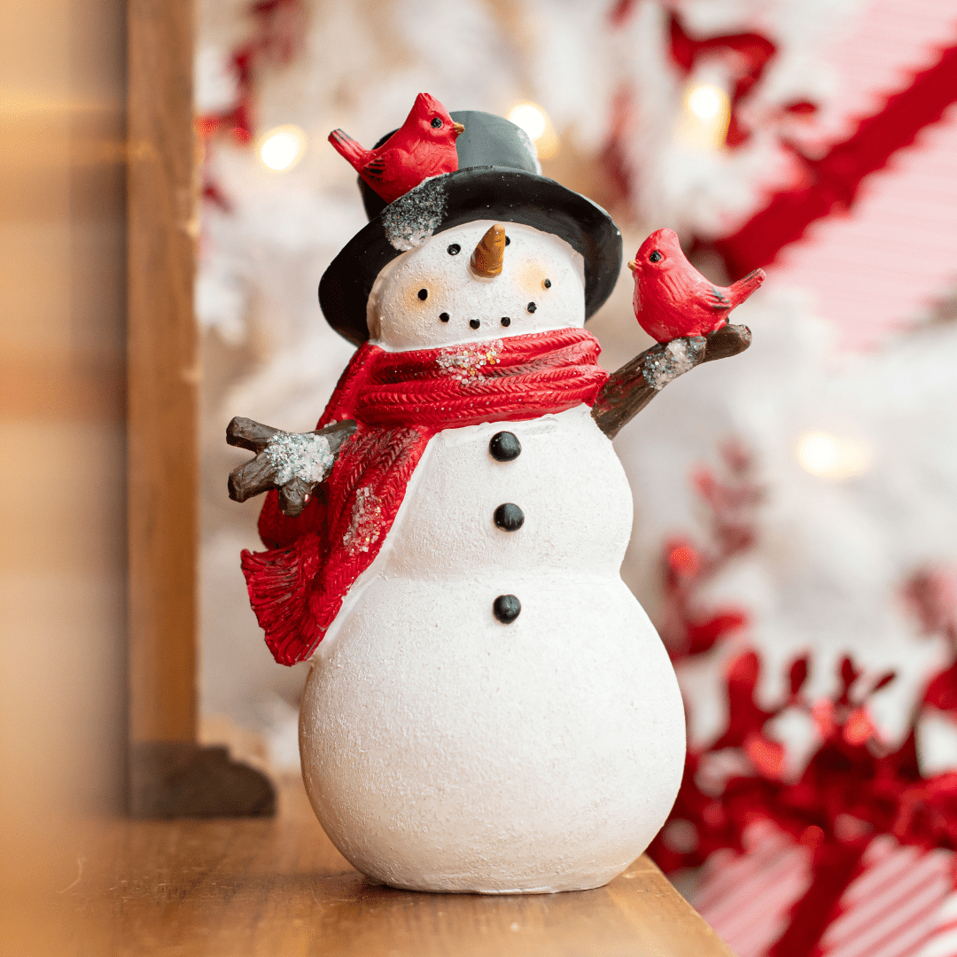 Festive snowman with red scarf and cardinals in front of Christmas lights for holiday decoration.