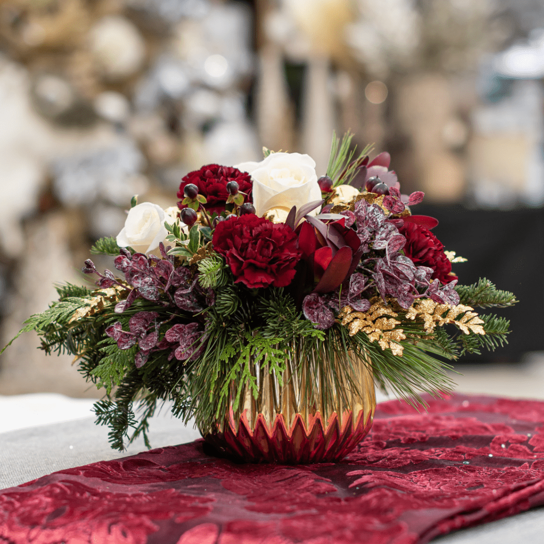 Elegant floral arrangement with red and white flowers in a gold vase, set on a rich red tablecloth.