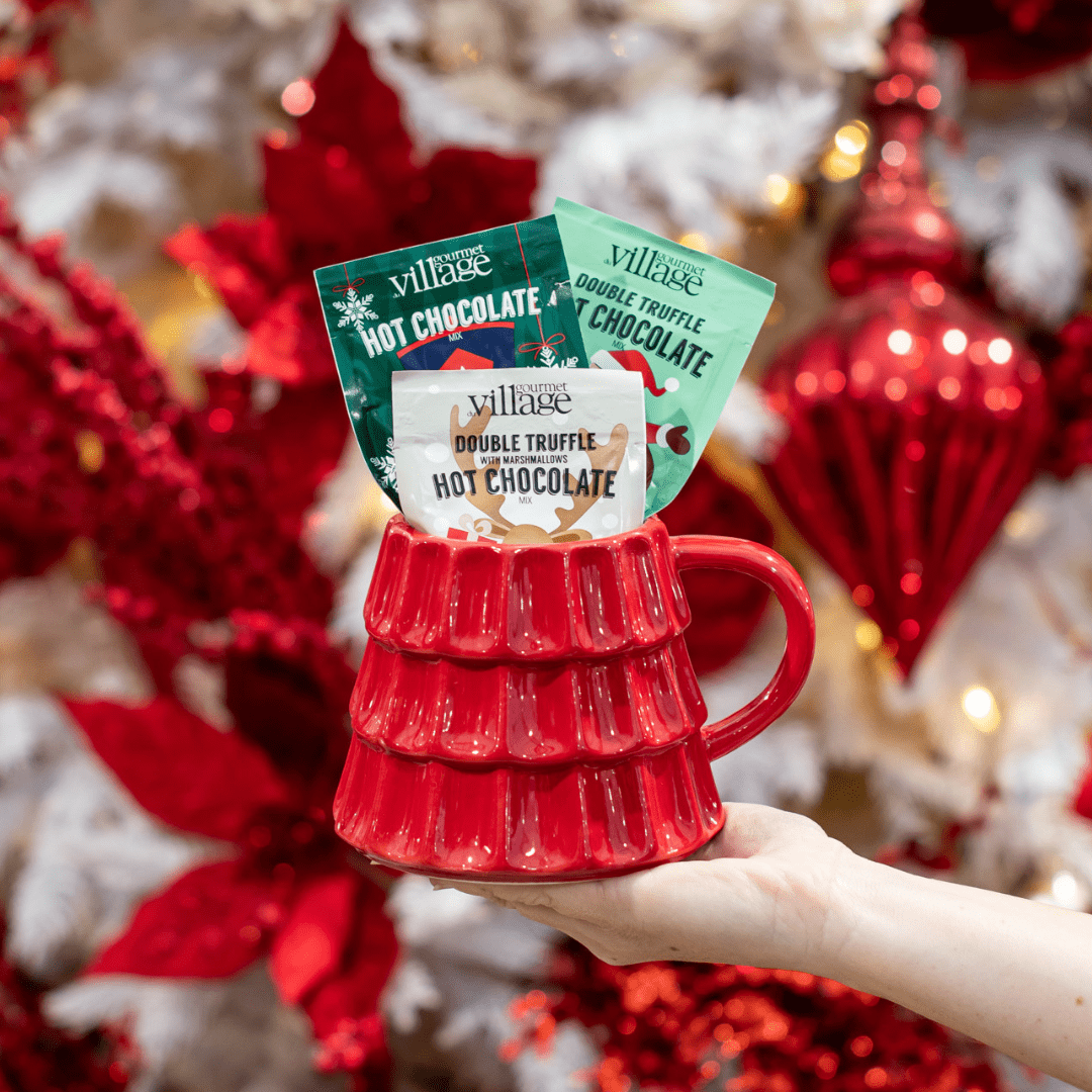 Festive red mug with hot chocolate packets, perfect holiday gift, surrounded by red and white Christmas decorations.