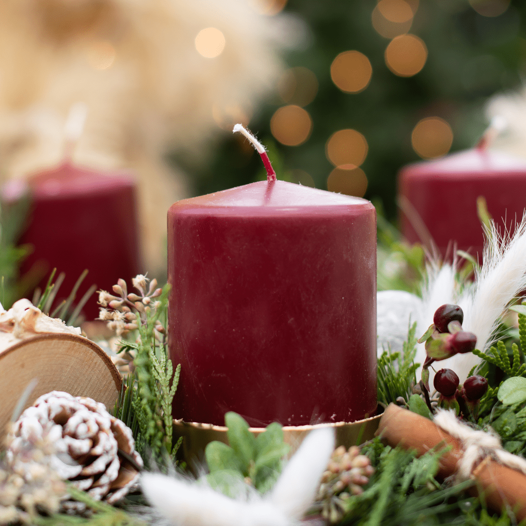 Red candle centerpiece with pinecones and greenery, set against blurred holiday lights for a festive ambiance.
