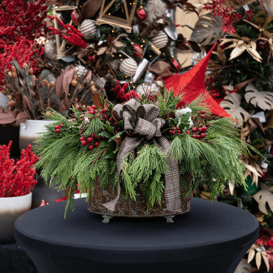 Design of the Day 2022 (7) Festive holiday centerpiece with greenery, pine cones, red berries, and a plaid bow on a black table.