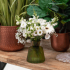 Elegant white flower bouquet in a green vase on wooden table with copper pots in the background.