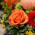Vibrant fall floral arrangement with orange rose, red gerbera, yellow flowers, greenery, and mini pumpkin.
