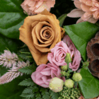 Close-up of a floral arrangement with orange rose, pink lisianthus, and greenery for a colorful bouquet.