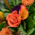 Close-up of a vibrant floral bouquet featuring an orange rose and calla lily surrounded by lush green leaves.