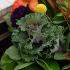 Colorful floral arrangement with ornamental kale, yellow billy button, and orange flowers.