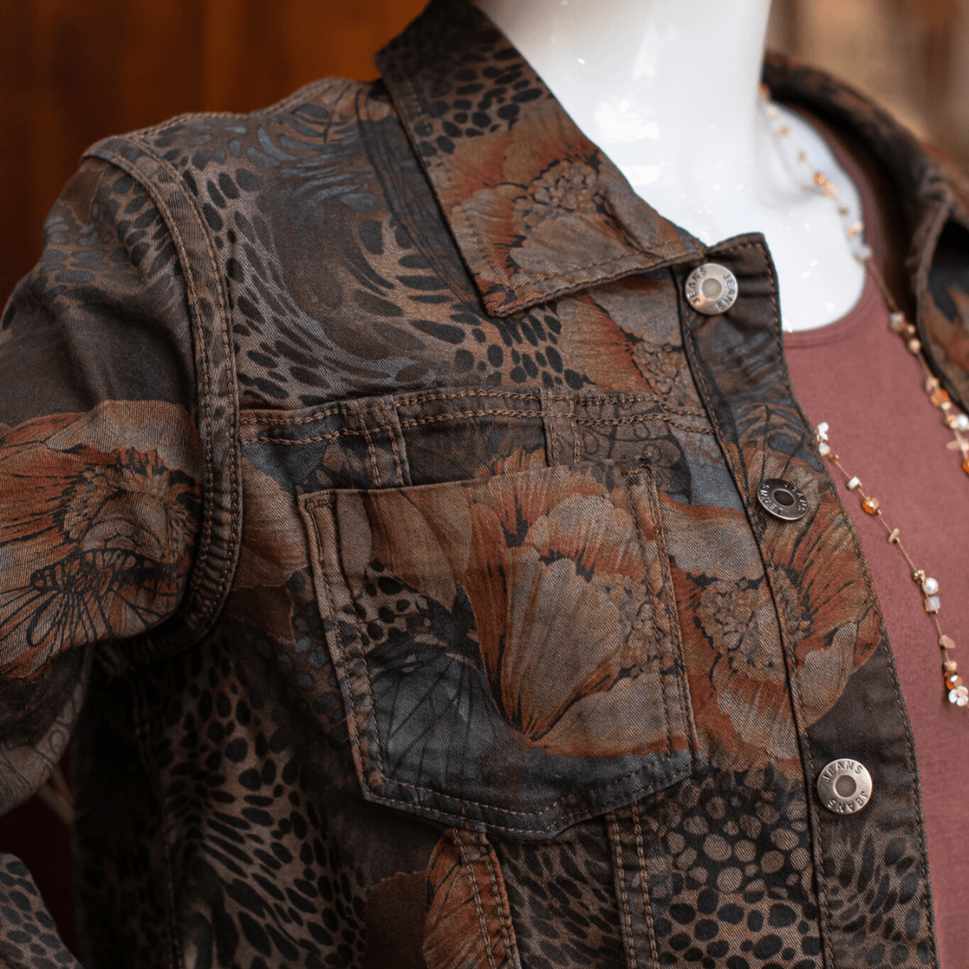 Floral-patterned denim jacket with earthy tones, displayed on a mannequin in stylish fashion setting.