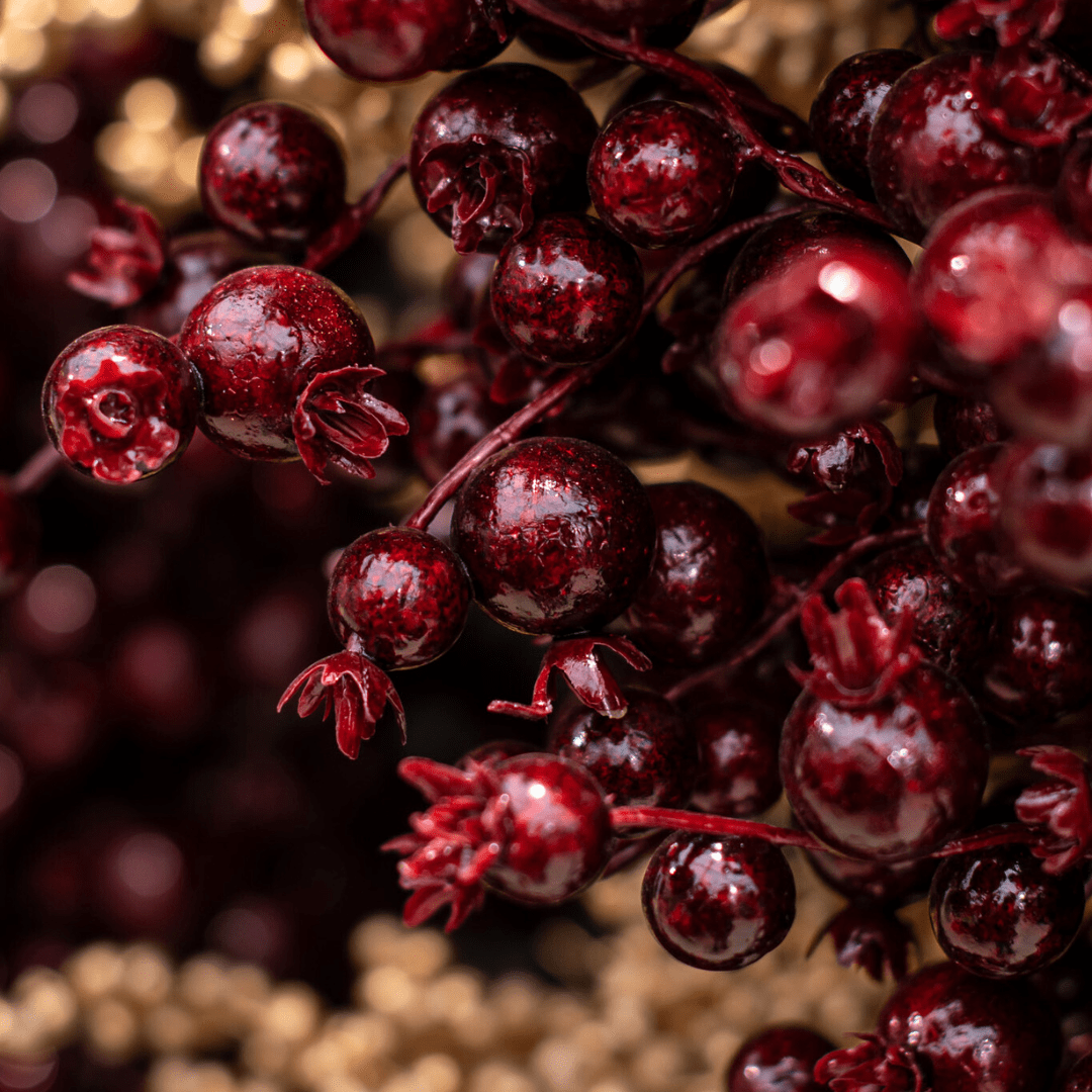 Close-up of shiny red berries with intricate details against a blurred background, creating a vivid and lush scene.