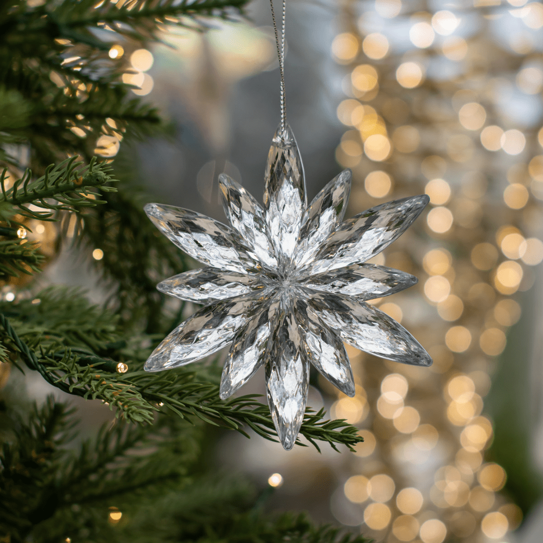 Sparkling crystal snowflake ornament hanging on a Christmas tree with festive lights in the background.