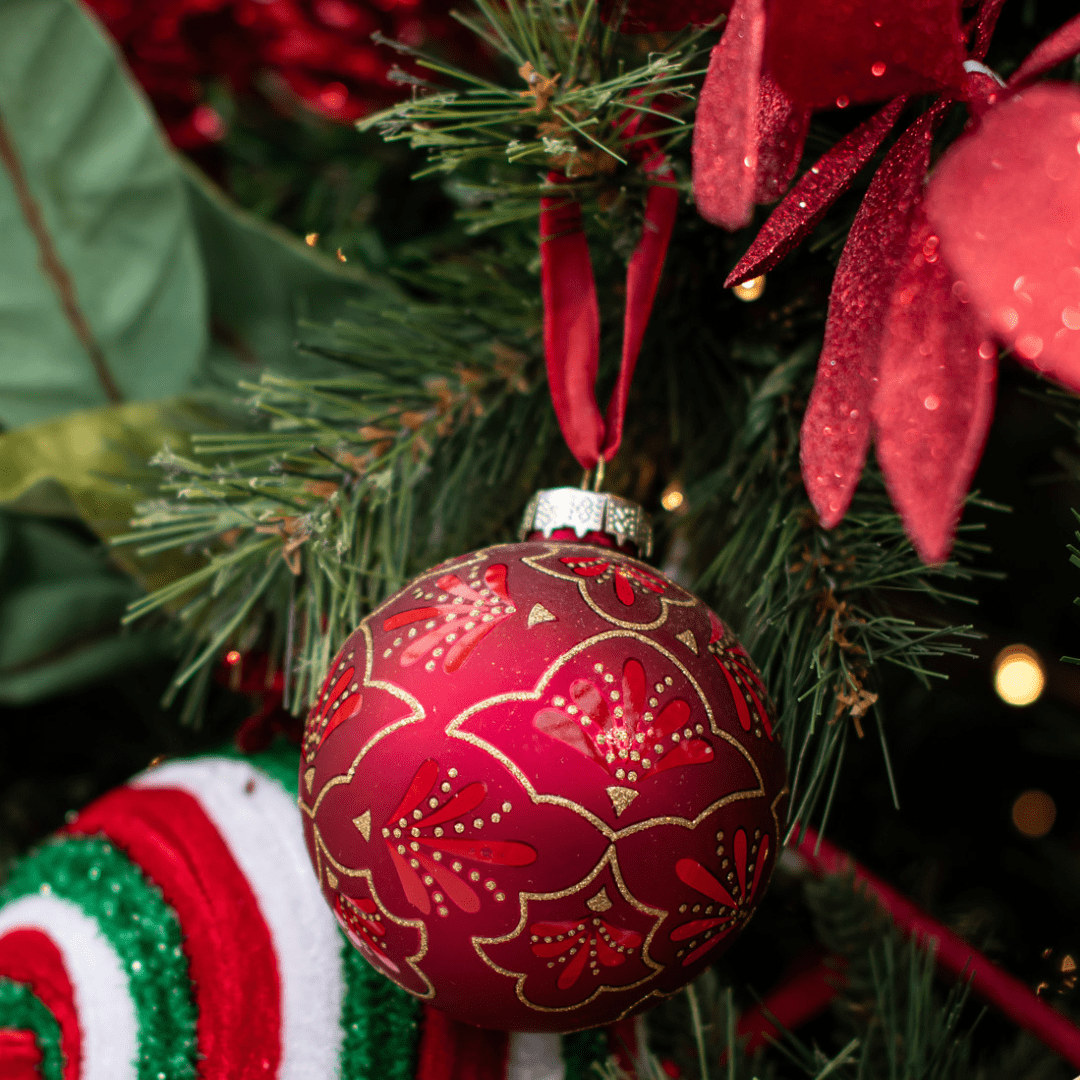 Festive red and gold Christmas ornament hanging on a decorated tree branch, highlighting holiday cheer.