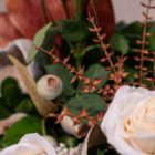 Vibrant floral arrangement with white roses, green leaves, red-orange accents, and decorative seed pods.