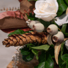 Close-up of a floral arrangement with a white rose, pinecone, and eucalyptus, featuring rich greenery and rustic elements.