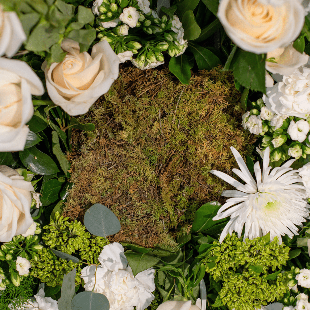 A lush floral arrangement with white roses, greenery, and moss centerpiece, perfect for a natural decoration theme.