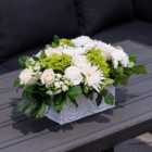 Elegant floral arrangement with white roses, chrysanthemums, and green accents in a rectangular white vase on a table.