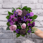 Beautiful bouquet of purple and pink flowers with green leaves against a white brick wall background.
