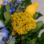 Yellow rose with vibrant yellow and blue wildflowers in a lush green bouquet.