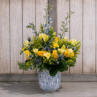 Elegant bouquet in blue vase with yellow and blue flowers against rustic wooden background. Perfect floral decor.