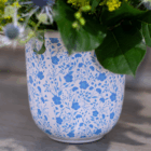 Decorative floral vase with blue pattern, filled with greenery and flowers on a wooden surface.