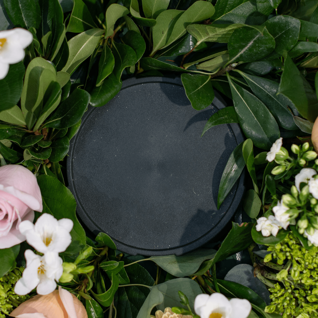 Empty circular tray surrounded by lush green leaves and flowers, perfect for garden decor or floral arrangements.