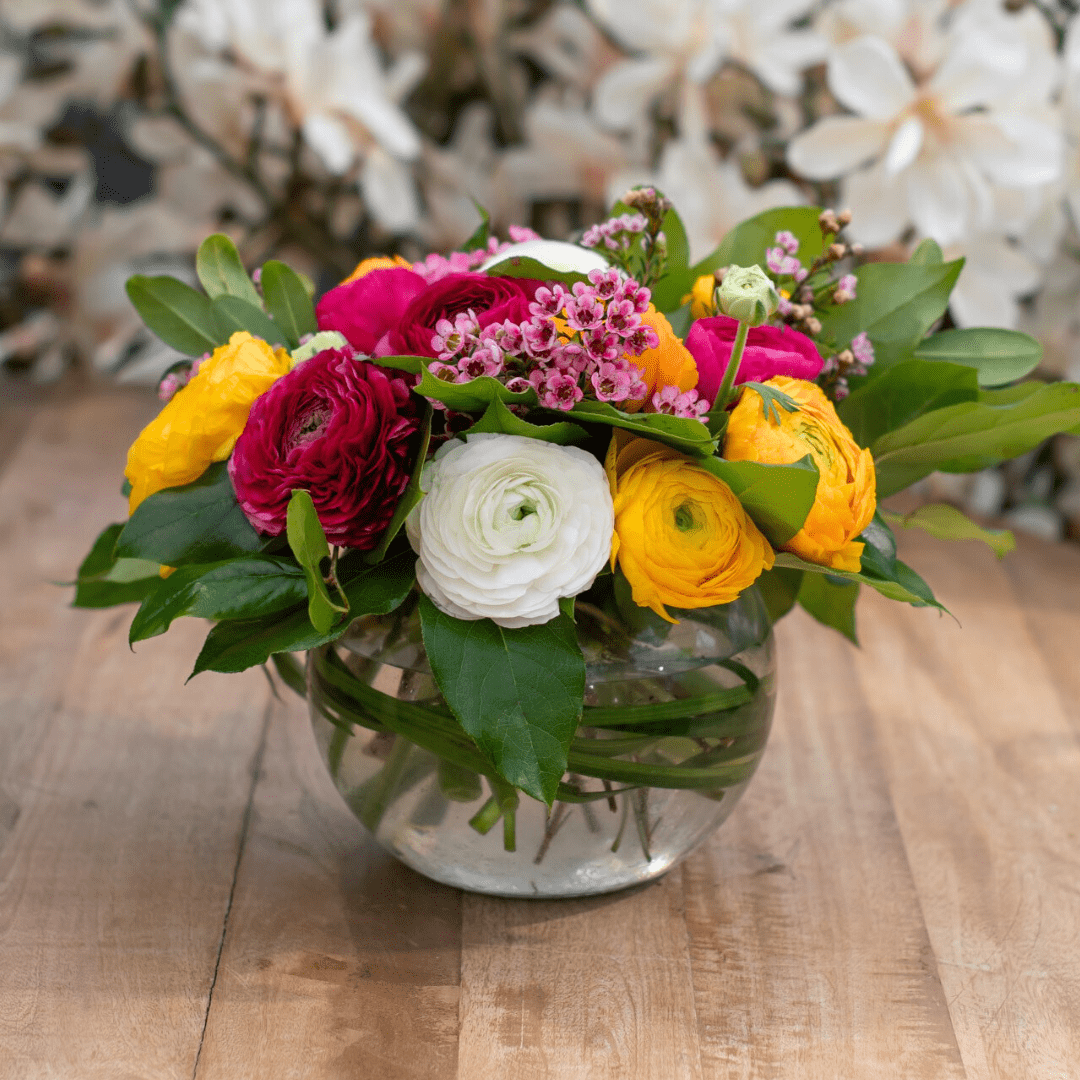 Vibrant floral arrangement with roses and greenery in a clear vase on a wooden table, perfect for spring decor.