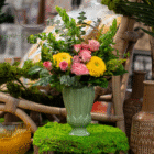 Green vase with pink roses and yellow flowers on a lush green surface, creating a vibrant and fresh display.