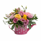 Colorful flower arrangement in pink floral watering can, featuring roses and gerbera daisies on a white background.
