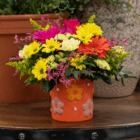 Vibrant bouquet of daisies and roses in a colorful flowerpot on a wooden table.