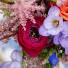 Vibrant bouquet with pink ranunculus, purple bellflowers, and orange accents showcasing colorful floral diversity.