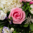 Close-up of a pink rose surrounded by white hydrangeas and greenery in a floral arrangement.