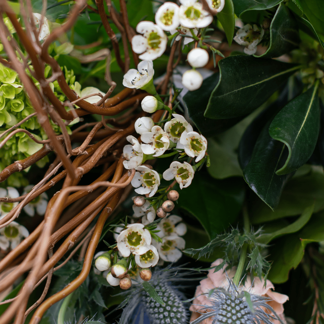 Close-up of a vibrant floral arrangement with white flowers, green leaves, and twisted brown branches.