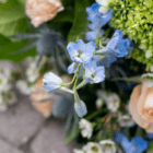 Delicate blue flowers with mixed greenery and peach roses create a vibrant, fresh bouquet.