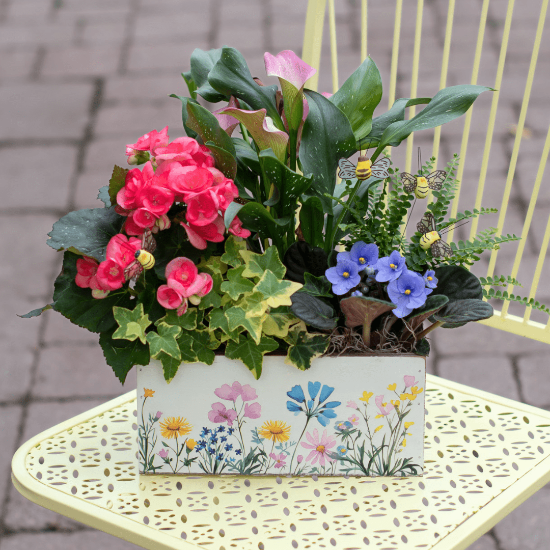 Colorful flower arrangement in a decorative planter on a yellow table, featuring pink and purple blooms with lush greenery.