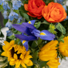 Vibrant bouquet with sunflowers, blue iris, orange roses, and blue delphiniums. Perfect for special occasions.